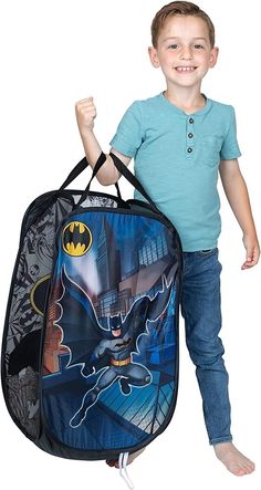 a young boy is holding a batman bag and smiling at the camera while standing in front of him