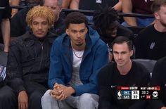 two young men sitting next to each other at a basketball game, one is wearing a blue jacket