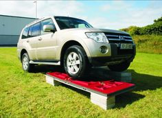 a silver suv is parked on top of a red object in the grass near a building