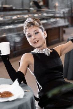 a woman sitting at a table with a coffee cup and saucer in her hand