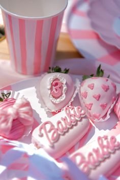 pink and white desserts are arranged on a plate next to a cup with strawberries in it