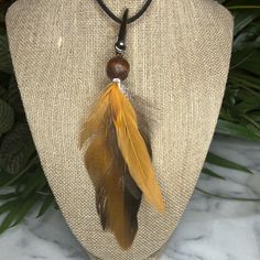 a necklace on a mannequin with a brown bead and feather charm hanging from it