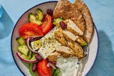 a plate with chicken, cucumbers, tomatoes and pita bread