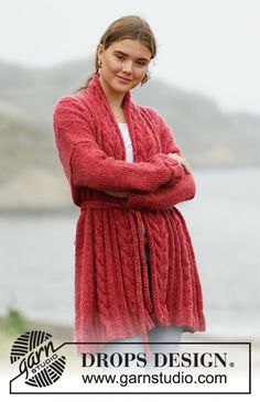 a woman wearing a red cardigan standing in front of the ocean with her arms crossed