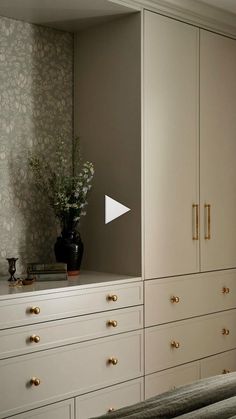 a bedroom with white drawers and gold handles on the doors, along with a vase filled with flowers