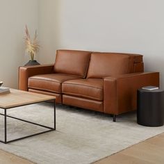 a brown leather couch sitting on top of a white rug next to a wooden table