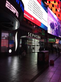 people are walking on the sidewalk in front of large billboards