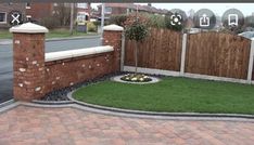 a brick fence and green grass in the middle of a driveway with flowers on it