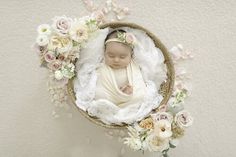 a baby in a basket surrounded by flowers and greenery on the side of a wall