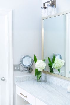 two white flowers are in a vase on the bathroom sink counter next to a mirror