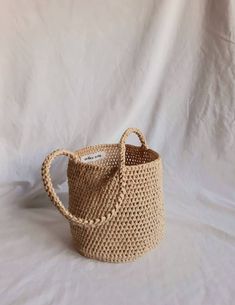 a small woven basket with handles on a white cloth covered tablecloth, ready to be used as a storage container