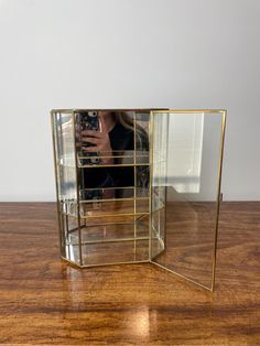 a woman taking a selfie in a mirror on top of a wooden table next to a wall