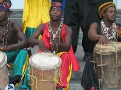 three men are sitting on the steps with their drums in front of them and one man is standing behind them