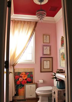 a white toilet sitting under a window next to a painting on the wall in a bathroom