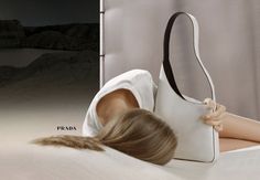 a woman laying on top of a bed next to a white purse with her head resting on the pillow