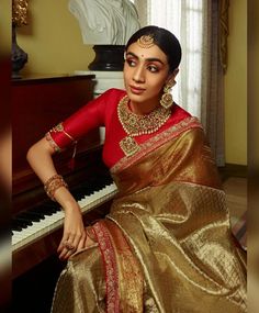 a woman in a red and gold sari sitting at a piano