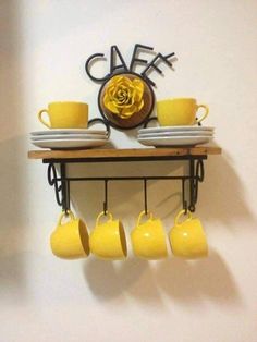 yellow coffee cups and saucers are hanging on a shelf with a clock above it