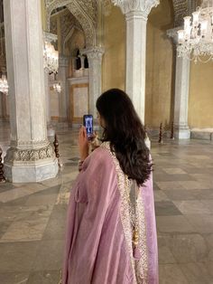 a woman in a pink outfit taking a photo with her cell phone inside a building