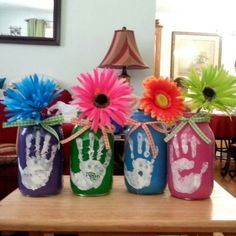 three painted mason jars with flowers and handprints on them sitting on a table