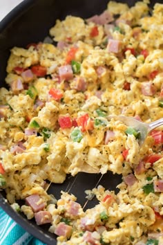 scrambled eggs with ham and vegetables in a skillet on a blue dish towel next to a wooden spoon