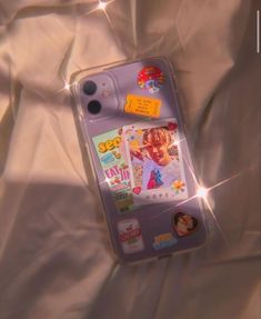 a cell phone laying on top of a bed covered in white sheets and stickers