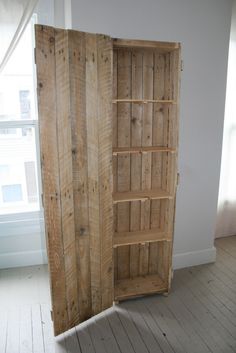 an open wooden bookcase sitting in the corner of a room next to a window