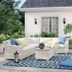 an outdoor living area with white wicker furniture and blue rug on the ground next to a house