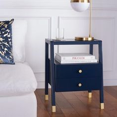 a night stand with two books on it next to a white couch and gold accents