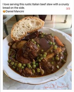 a white plate topped with meat and vegetables covered in gravy next to a slice of bread