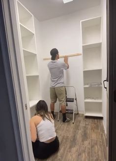 a man and woman are working on the walls in a room with white shelving