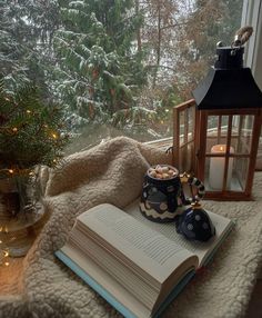 an open book sitting on top of a table next to a christmas tree and lantern