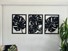 three black metal wall art pieces hanging on a white wall next to a green plant