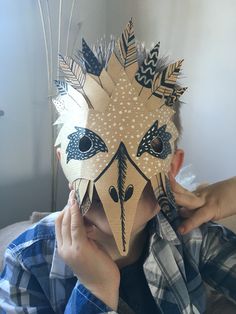 a person is covering their face with a mask made out of cardboard and feathers on it