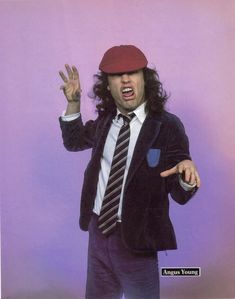 a man with long hair wearing a suit and tie, holding his hand up in the air