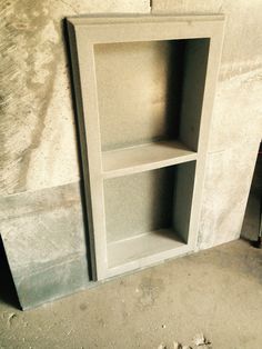 an empty book shelf in the corner of a room with concrete walls and flooring