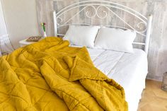 an unmade bed with yellow blankets and pillows on it in a bedroom area next to a wooden wall