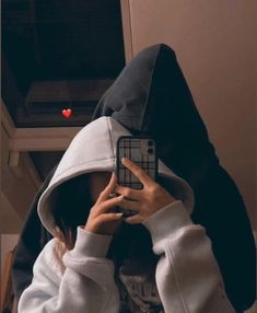 a person wearing a hoodie taking a selfie with their cell phone in the dark