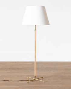 a floor lamp with a white shade on the base and a wooden stick in front of it