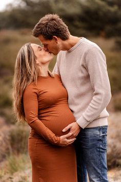 a pregnant couple kissing while standing in the grass