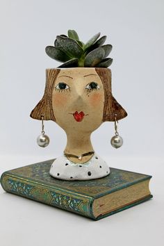 a planter with a woman's head and earrings on top of a book