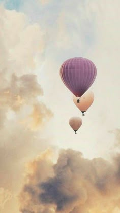 two hot air balloons flying in the sky with clouds behind them and one balloon is floating upside down