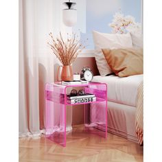 a pink table with an alarm clock on it in front of a bed and window