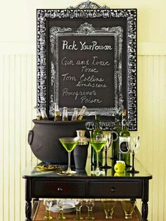 a black table topped with lots of bottles and glasses next to a chalkboard sign