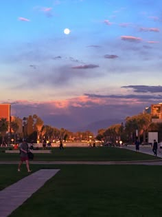 a person is flying a kite in the park at sunset or dawn with other people walking and sitting around