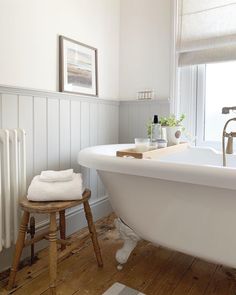 a white bath tub sitting next to a wooden stool in a bathroom under a window