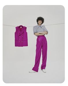 a man standing next to a pink shirt and purple pants on a clothes line with his arms crossed