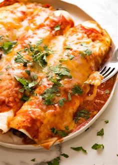 a white plate topped with lasagna covered in cheese and parsley next to a fork