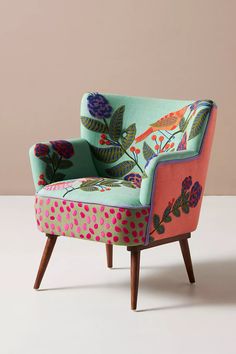 an upholstered chair with colorful flowers and birds painted on the back, sitting in front of a pink wall