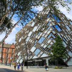 people walking on the sidewalk in front of a building that is shaped like a triangle