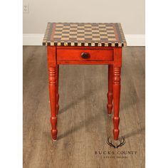 a small red table with checkered top and legs on wooden floor next to white wall